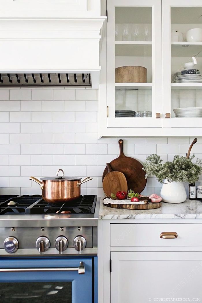 Modern kitchen featuring a stainless steel stove with blue oven, copper pot, and fresh decor on marble countertops.