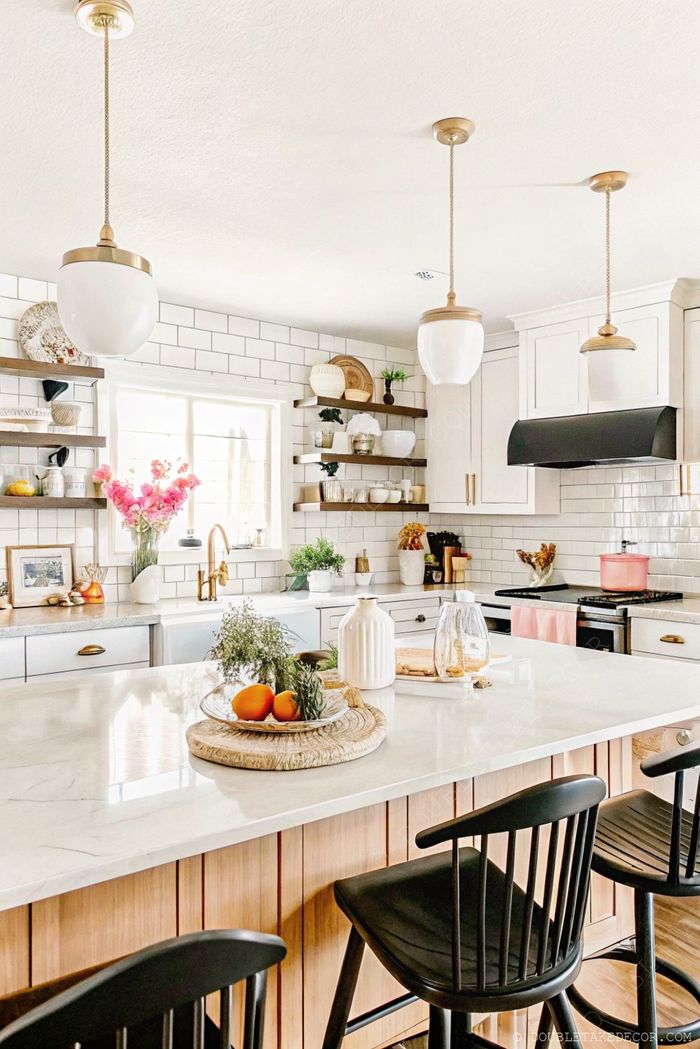 Stylish kitchen featuring marble island countertop with fruit tray, pendant lighting, and decorative floating shelves with plants and ceramics.