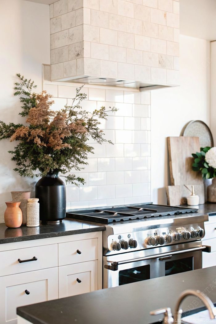 Modern kitchen with stainless steel range, decorative floral arrangement in black vase, and ceramic pots adding character to the countertop.
