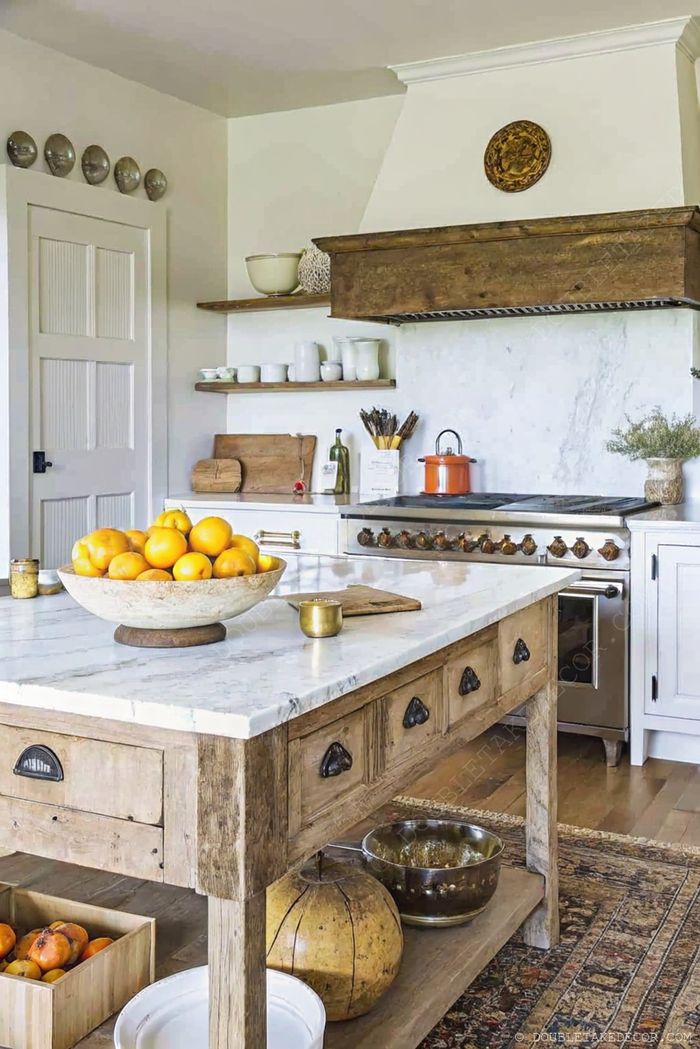 Marble-topped kitchen island with fresh oranges, surrounded by wooden accents, open shelving and modern appliances in a warm neutral palette.