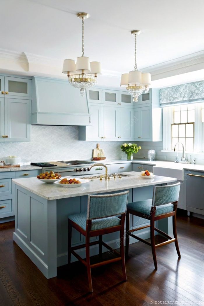 Modern kitchen featuring soft blue cabinets, a marble island with fresh fruit, crystal pendant lights, and stylish blue striped bar stools.