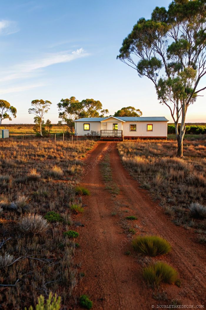 A contemporary single-story modular home with flat roof nestled in serene countryside at sunset, featuring a welcoming porch and natural landscaping.
