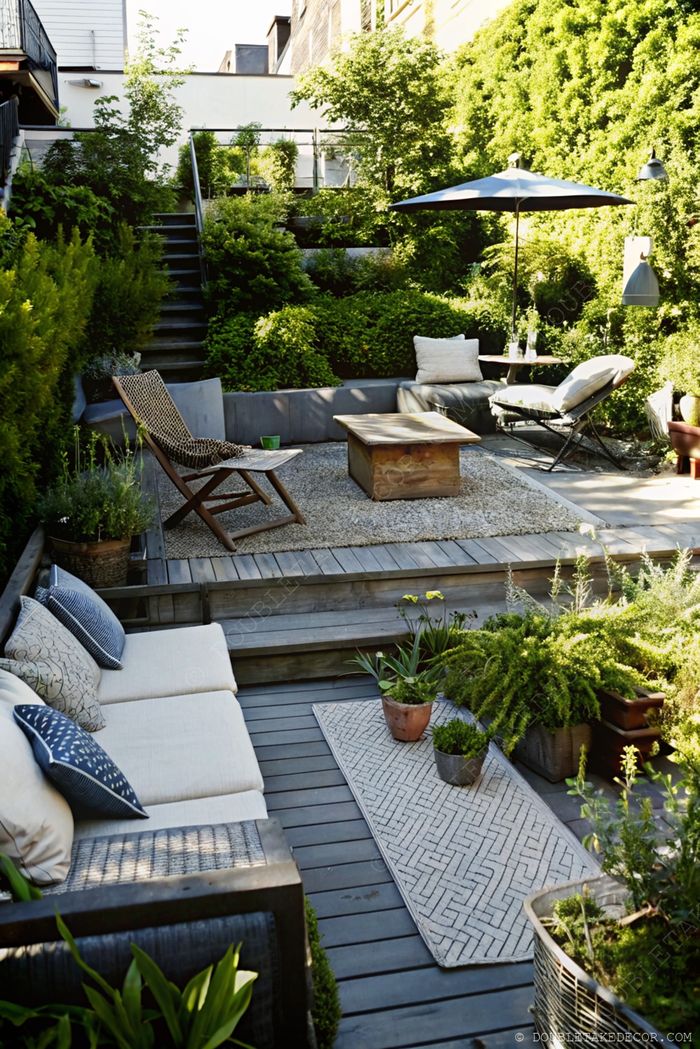Terraced outdoor living space with gray sectional sofa, wooden coffee table, and lush greenery creating a tranquil retreat.