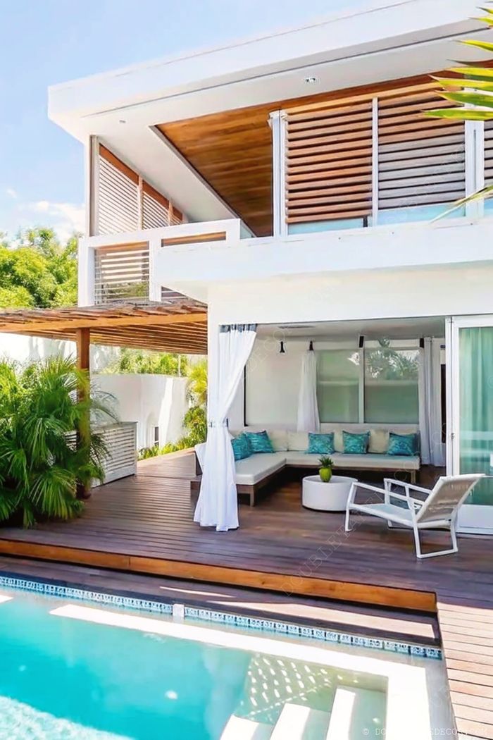 Modern outdoor living space with wooden deck, pool, turquoise cushioned sectional sofa, and white pergola curtains creating a luxurious retreat.
