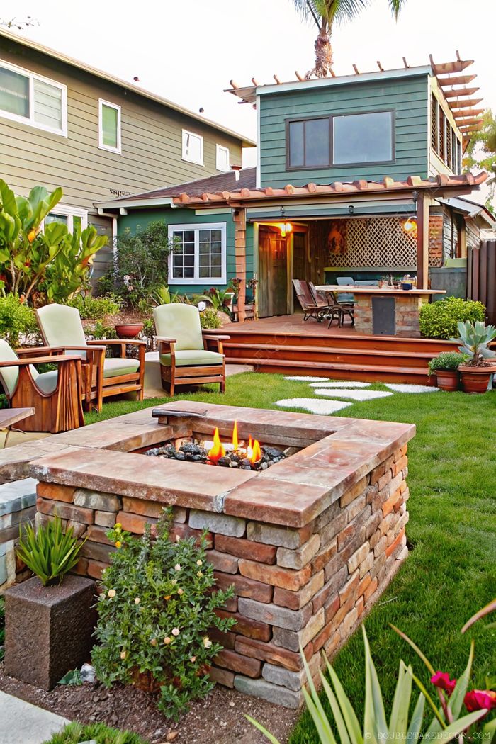 Stone fire pit with wooden chairs creating an inviting outdoor gathering space near a deck with dining area and lush greenery.