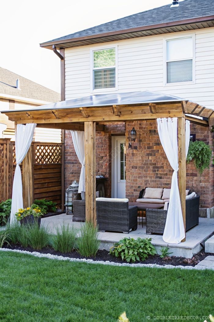 Wooden pergola with metal roof, white curtains, and wicker furniture creating a stylish, comfortable outdoor living space.