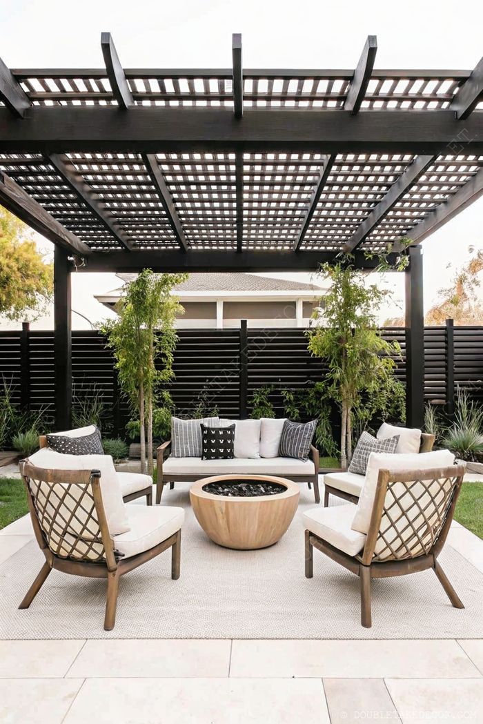 Elegant outdoor living space with wooden pergola, round fire pit, and comfortable seating against a modern black slatted fence.
