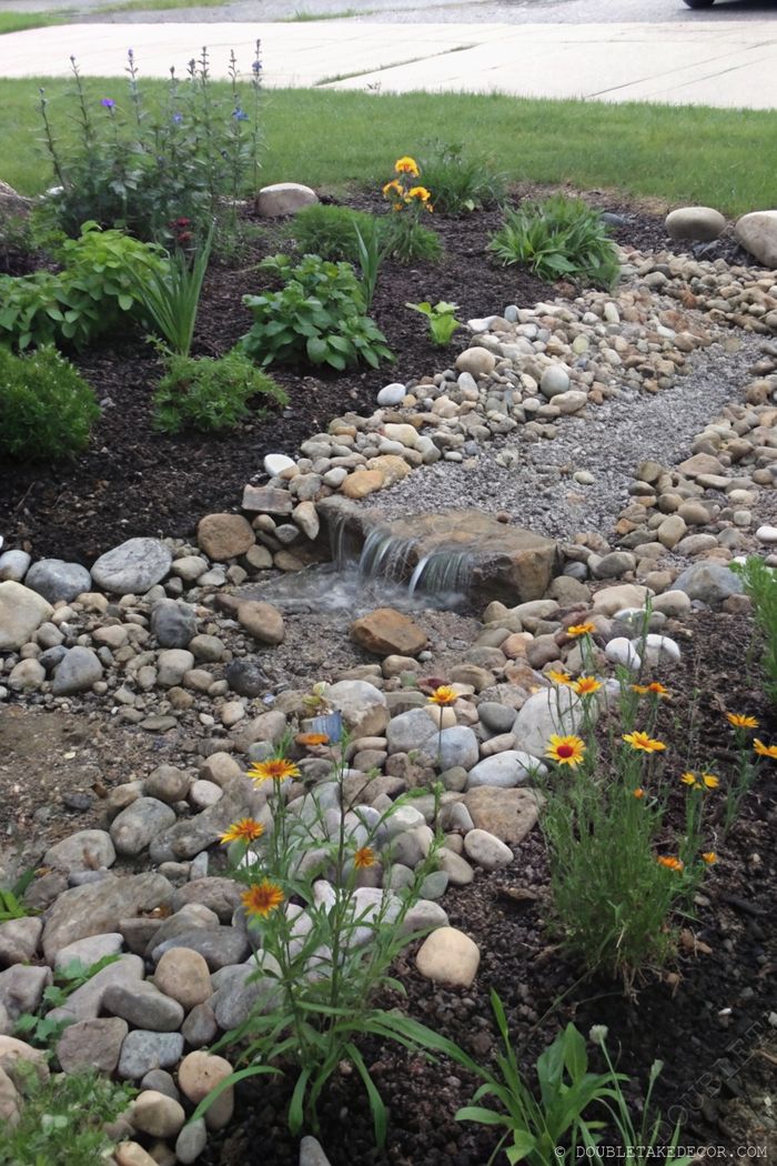 Serene garden landscape with cascading water feature, vibrant yellow flowers, lush greenery, and pebble pathway promoting relaxation and biodiversity.