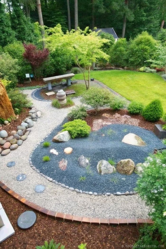 A tranquil garden with a stone bench surrounded by lush greenery, featuring a meandering gravel and pebble path amid ornamental plants.