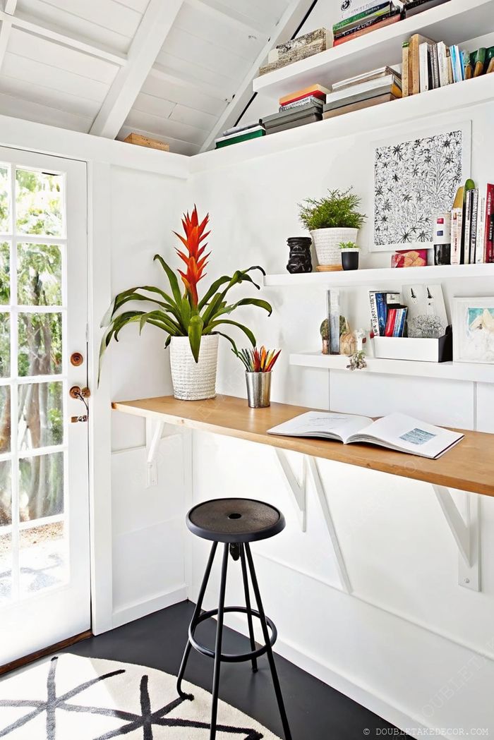 Cozy workspace with light wood desk, black stool, and vibrant plants creating an inviting she shed office retreat.