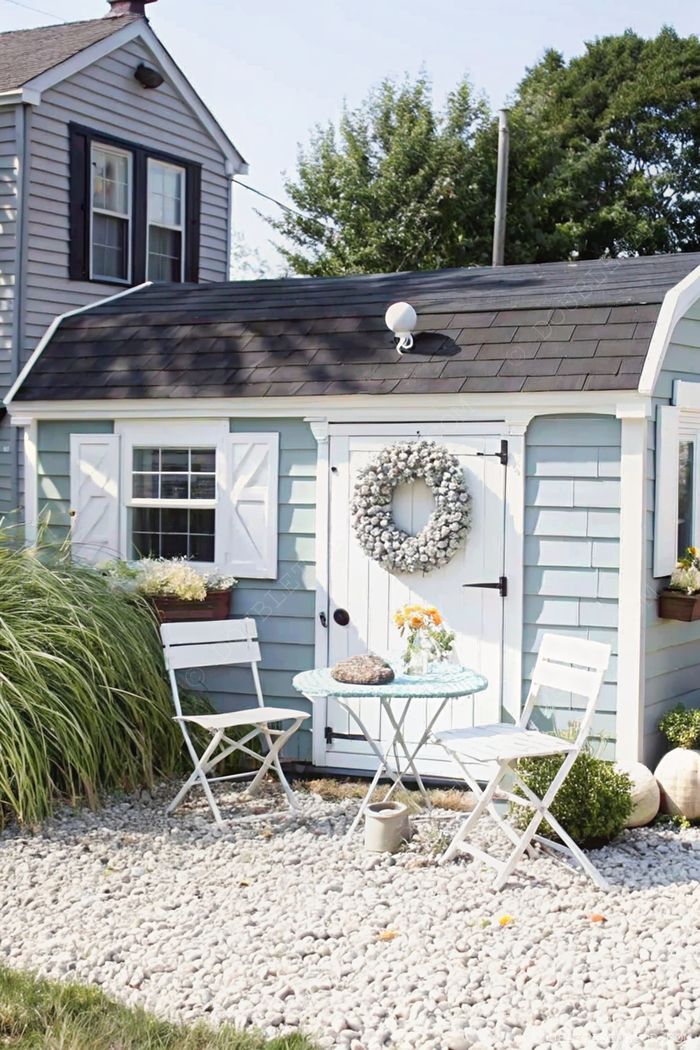 Blue shed with white trim, decorative wreath, and flanking shutters featuring an inviting bistro setup for relaxation.