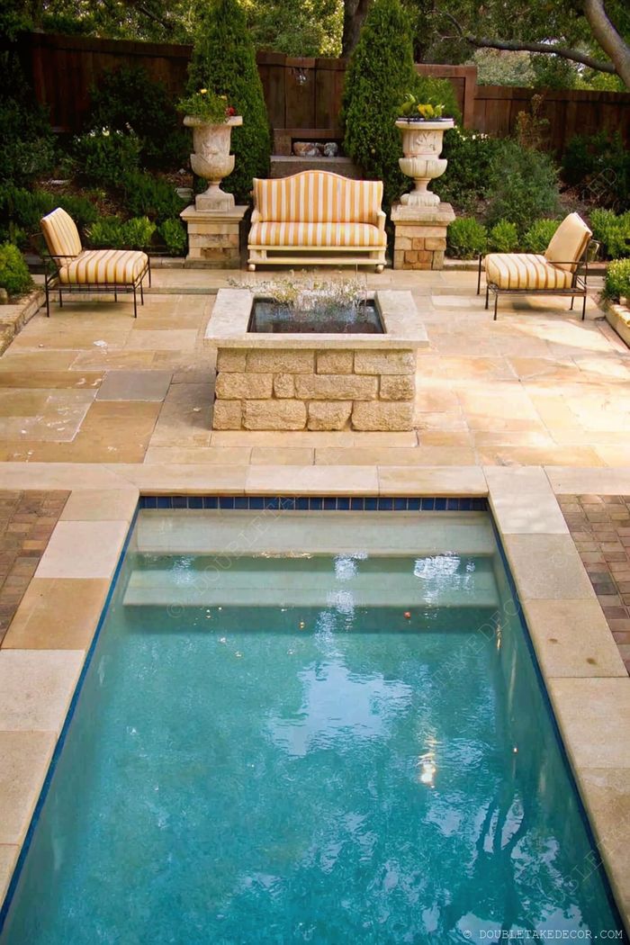 Rectangular swimming pool with stone pavers surrounded by cream and yellow striped outdoor furniture and decorative planters.