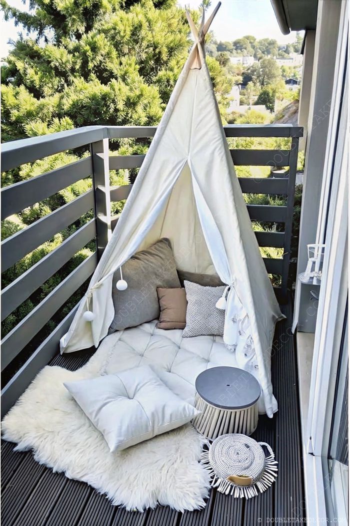 White teepee tent on a balcony with plush cushions, quilted mat, and small table creating a serene outdoor relaxation nook.