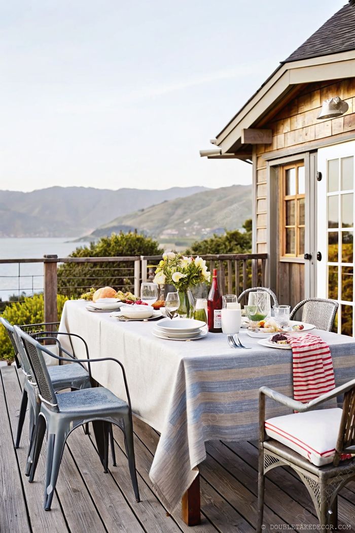 Elegant outdoor dining area on a wooden deck with a striped tablecloth, fresh food, and beautiful views of rolling hills and water.