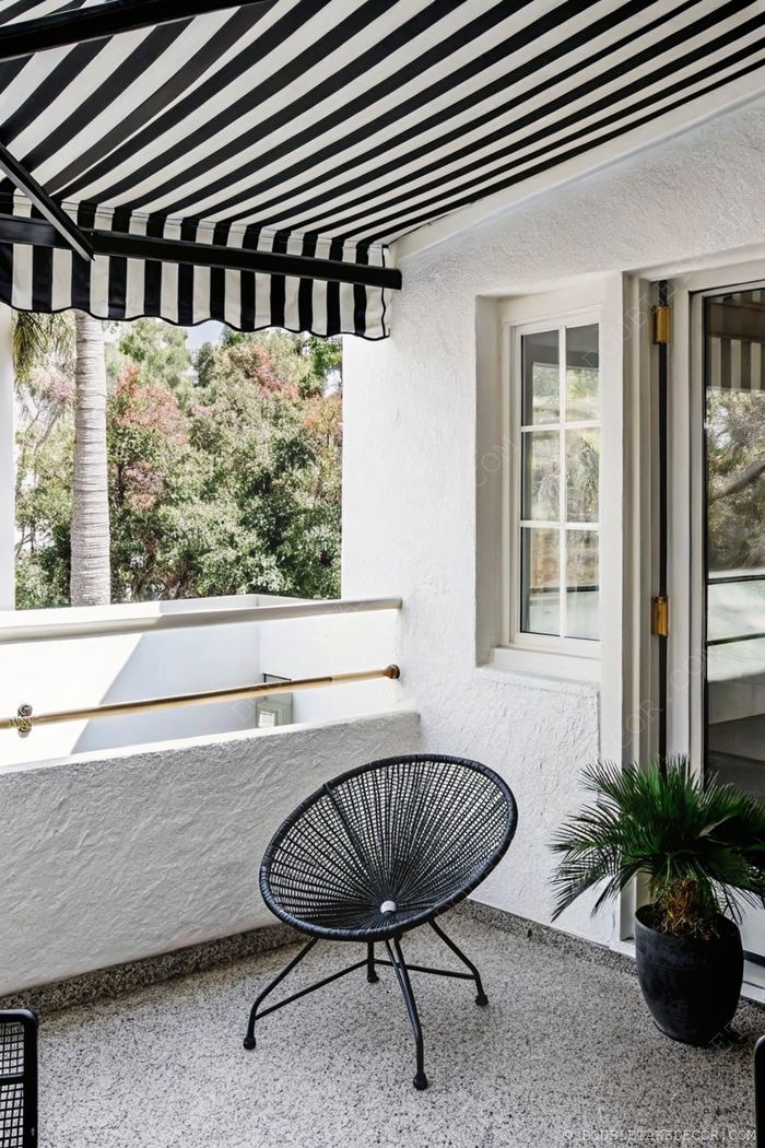 Stylish balcony with black and white striped awning, modern Acapulco chair, and potted greenery against white walls and gray flooring