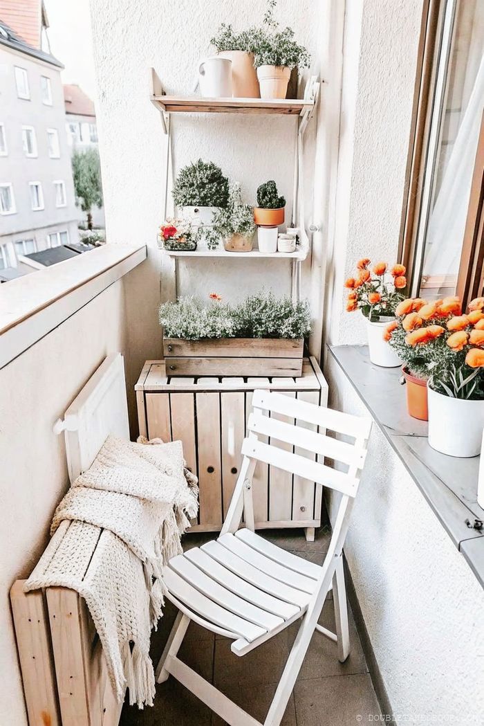 Charming balcony featuring wooden furniture, potted plants on shelves, and bright orange flowers creating a cozy natural retreat.