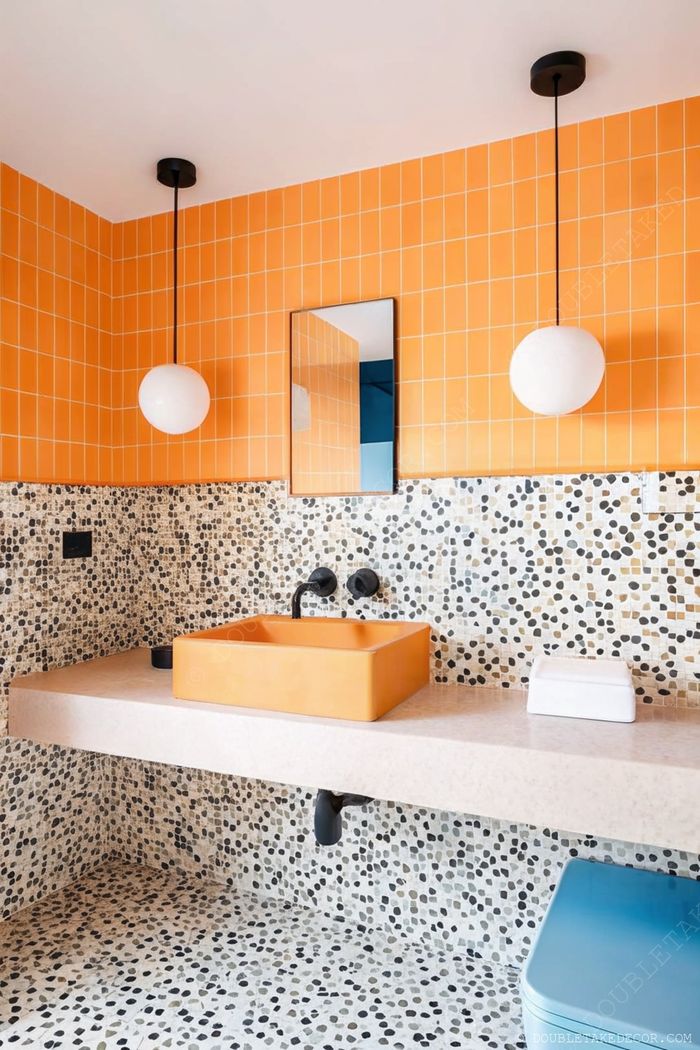 Salle de bain moderne avec carrelage orange éclatant, surfaces en pierre texturée, applique minimaliste et vasque carrée orange avec robinet noir.