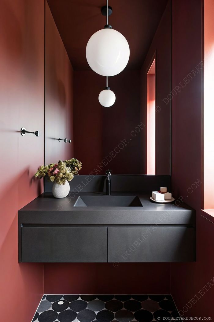 Salle d’eau moderne avec murs rouges profonds, plan de travail sombre, vasque carrée, robinet noir, suspensions et carrelage à motifs.