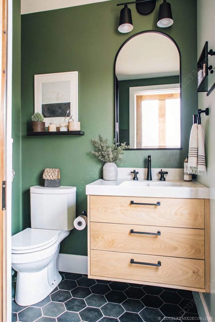 Petite salle de bain moderne avec murs vert intense, meuble en bois clair, robinets noirs et sol en tuiles hexagonales avec plantes décoratives.