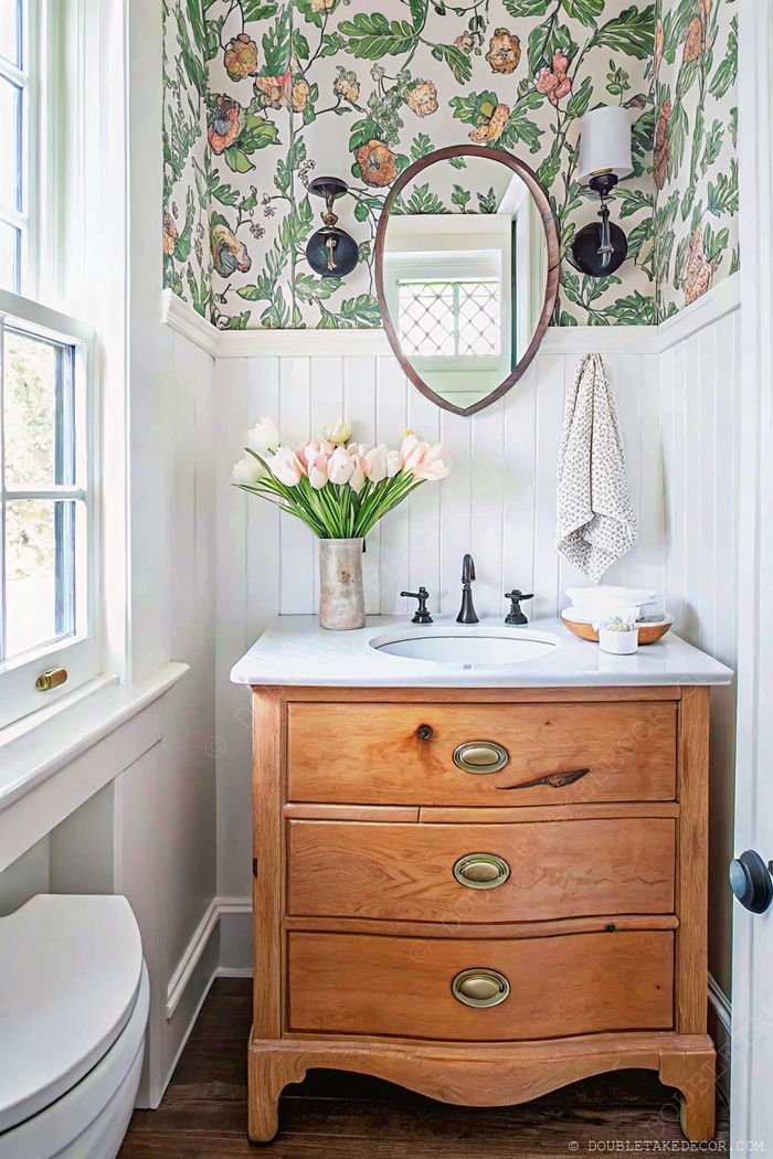 Petite salle d’eau avec papier peint à fleurs colorées, lavabo en marbre blanc, meuble en bois et tulipes fraîches pour un look lumineux et élégant.