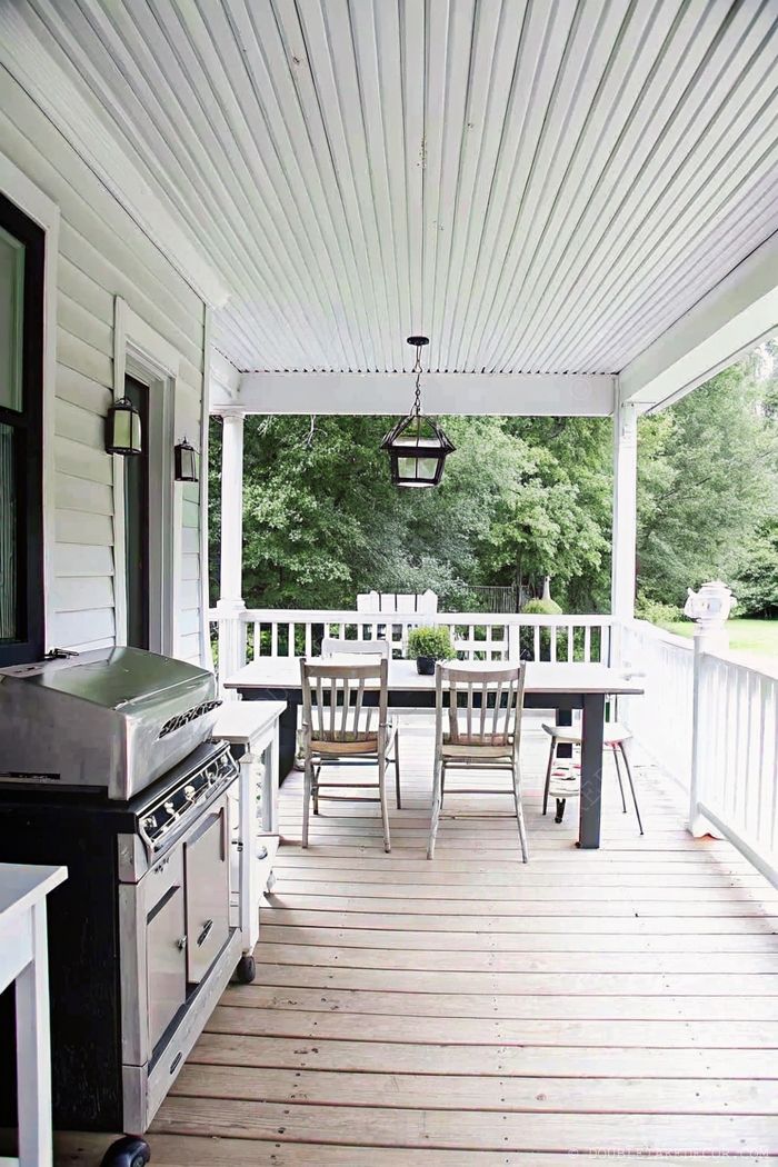 Charming wooden porch with white railings, featuring a dining table, chairs, pendant light, and grill for perfect outdoor entertaining.
