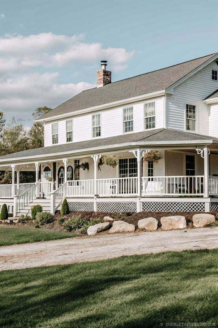 Charming two-story white house featuring a traditional wraparound porch with elegant railings, hanging planters, and a well-maintained green lawn.