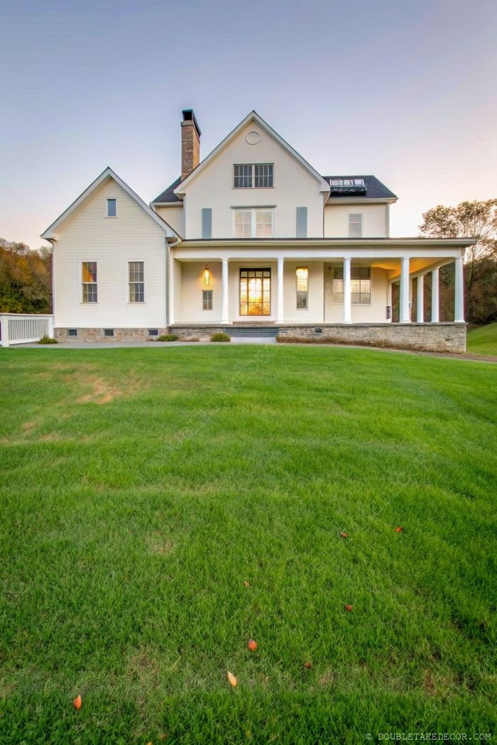 Spacious two-story house with white columns supporting a beautiful wraparound porch, nestled in lush green landscape