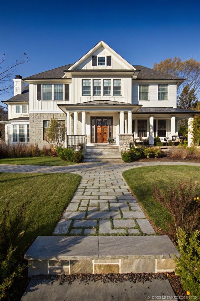 Contemporary home with white siding, stone elements, columned wraparound porch, and a beautifully landscaped pathway leading to wooden double doors.