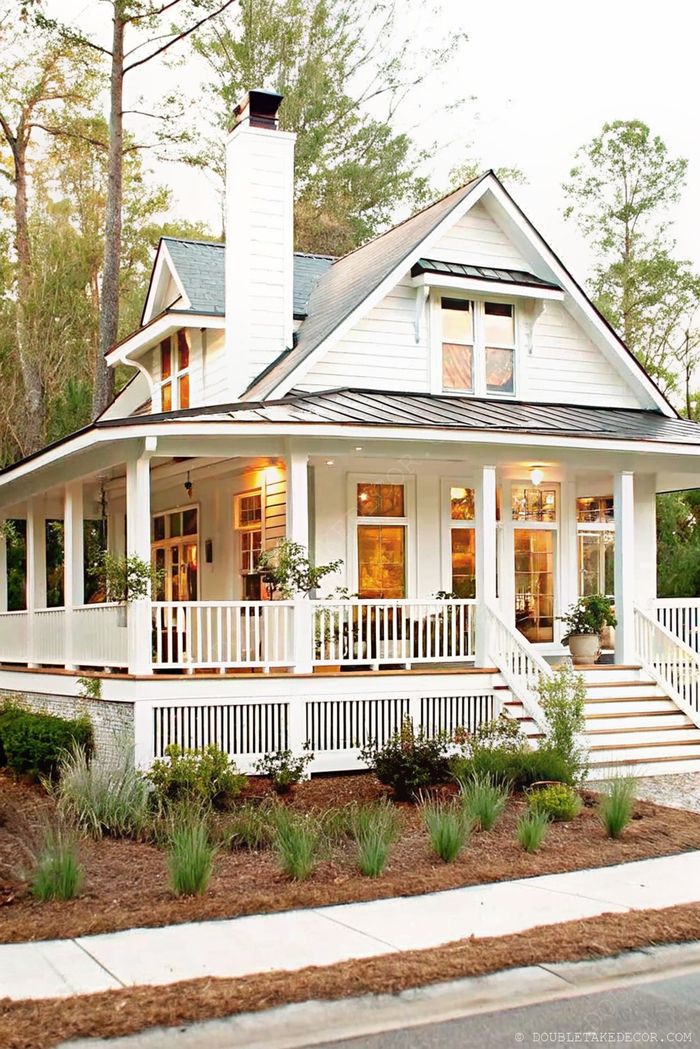 Two-story house with spacious wraparound porch, white railings, potted plants, and welcoming landscaped pathway