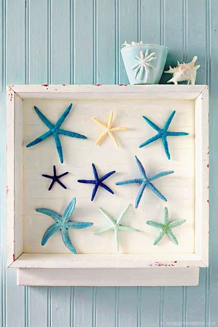 Rustic white frame displaying vibrant starfish in blue, yellow, and green tones against a soft blue background, creating nautical wall art.