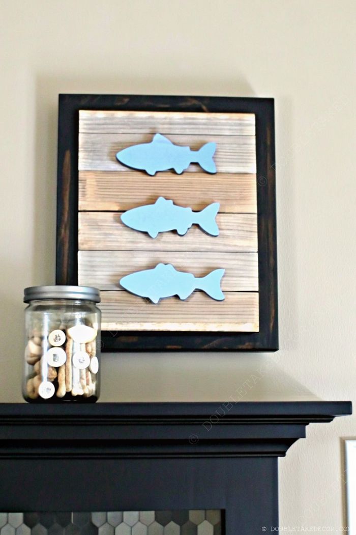 Soft blue fish silhouettes mounted on weathered wood, framed in black, with a coastal-themed glass jar beneath, creating charming nautical decor.