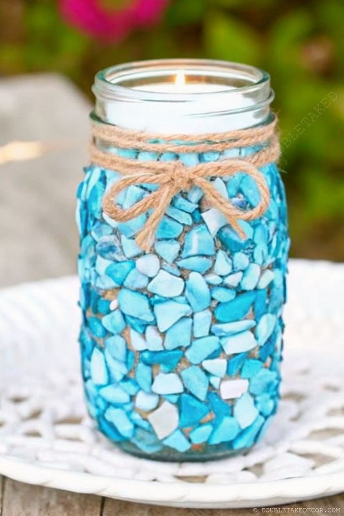 DIY nautical decor featuring a jar adorned with blue and white mosaic pieces, topped with a candle and rustic twine bow.