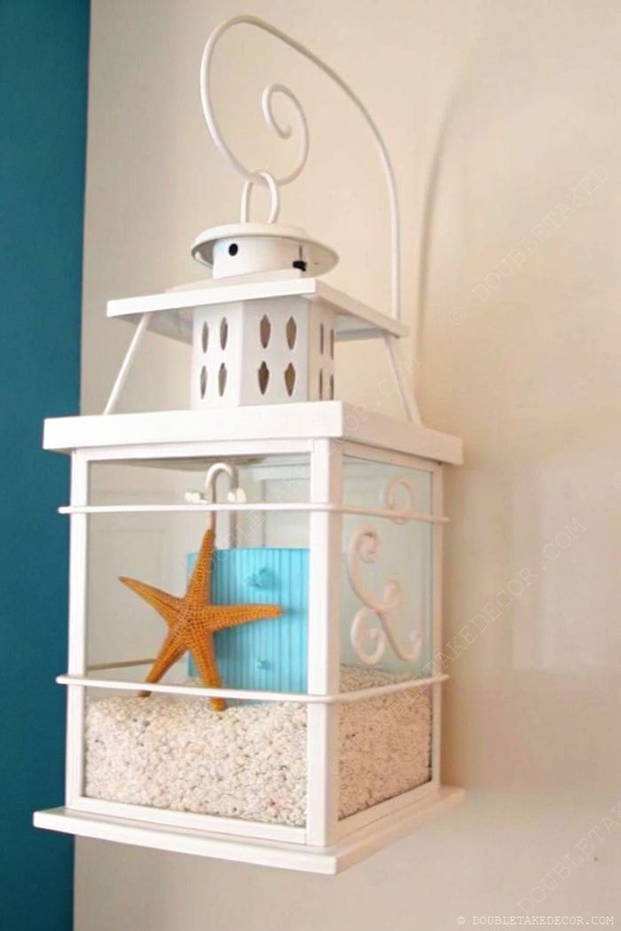 White coastal lantern with blue accent and vibrant orange starfish on decorative sand, hung against a light wall with blue contrast.