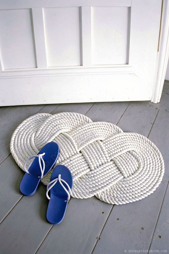Circular white braided rope doormat with blue flip-flops beside it, creating a coastal welcome on light gray wooden flooring.