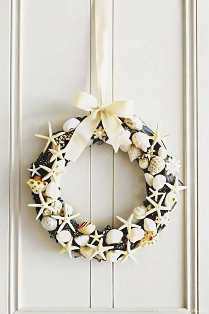 Coastal-themed circular wreath adorned with white and cream seashells, natural starfish, and a cream ribbon bow for hanging