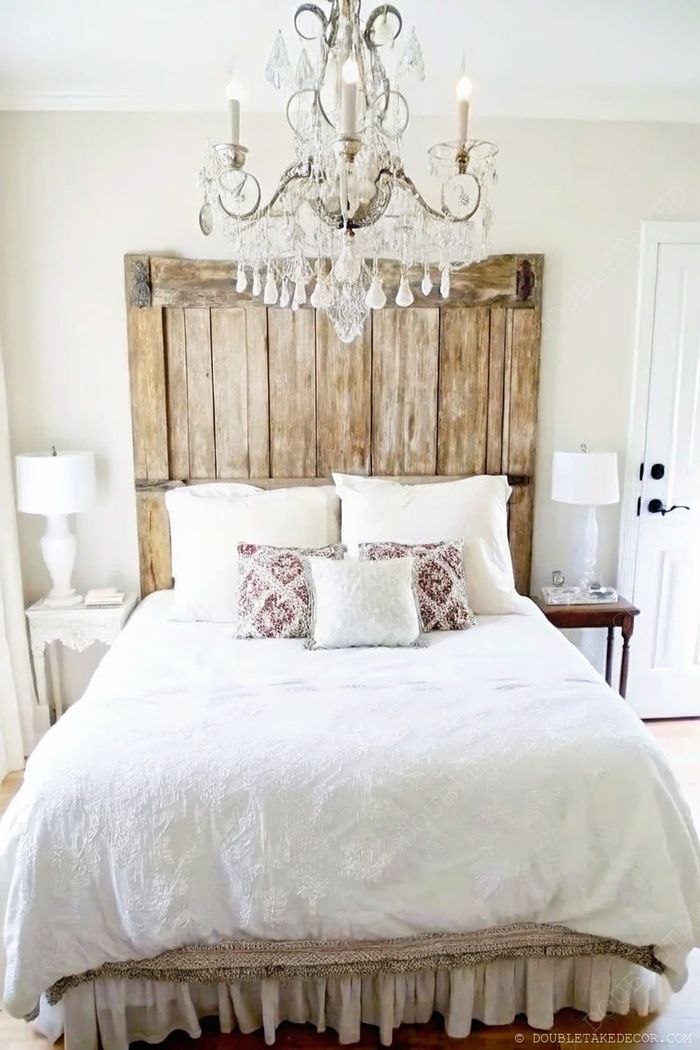 Bedroom with rustic reclaimed wood headboard, white embroidered duvet, crystal chandelier, and elegant bedside lamps creating a serene atmosphere.