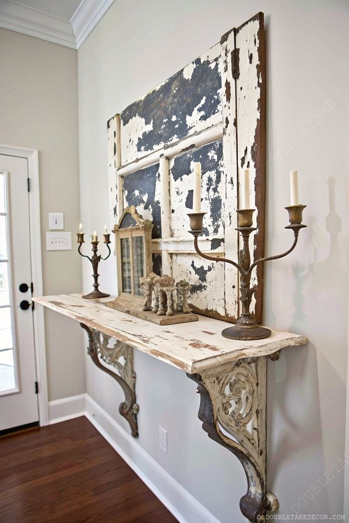 Weathered white console table with metal legs beneath a distressed blue-white panel, adorned with elegant candles and vintage accessories.
