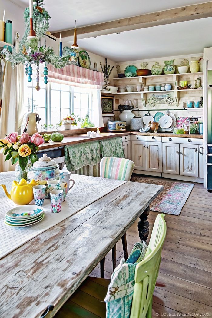 Cozy shabby chic kitchen with distressed cabinets, wooden table set with colorful dishware and roses, and open shelving for eclectic display.