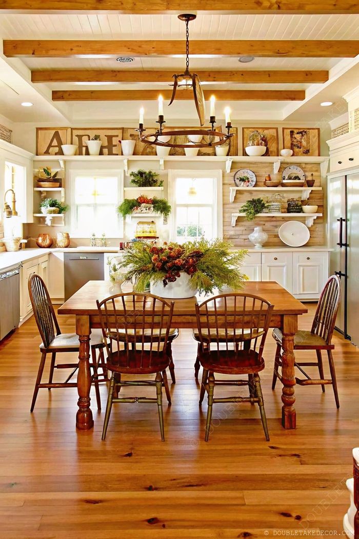 Inviting farmhouse kitchen featuring wooden dining table, rustic chandelier, open shelving with white dishware, and warm natural light.