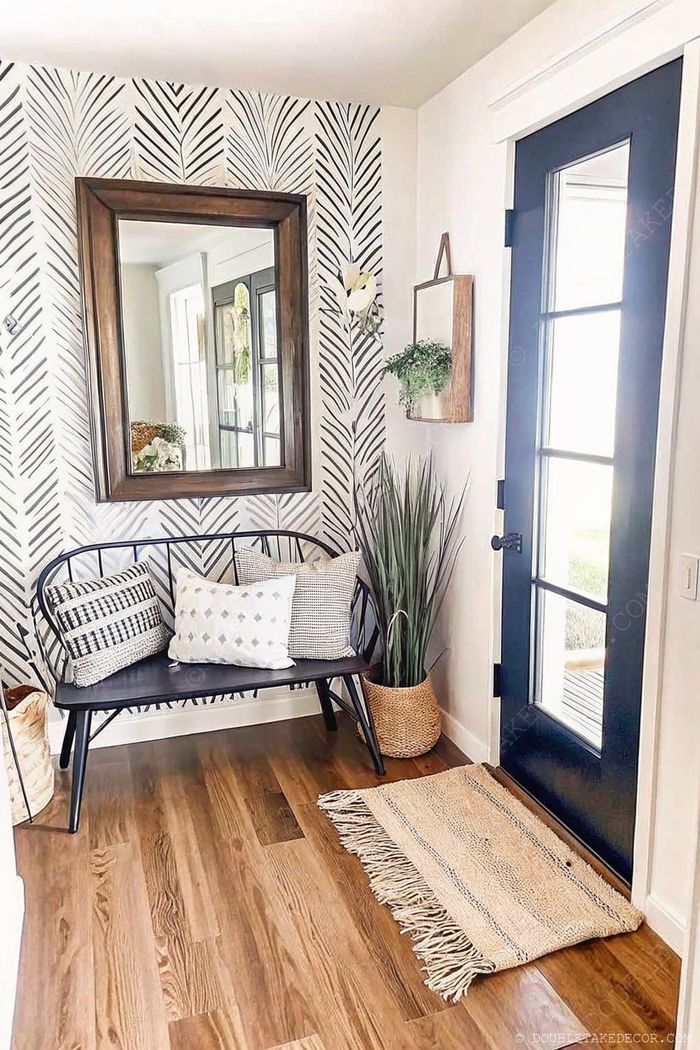 Stylish farmhouse entryway featuring wooden-framed mirror, black-and-white wallpaper, black bench with pillows, and greenery accents.