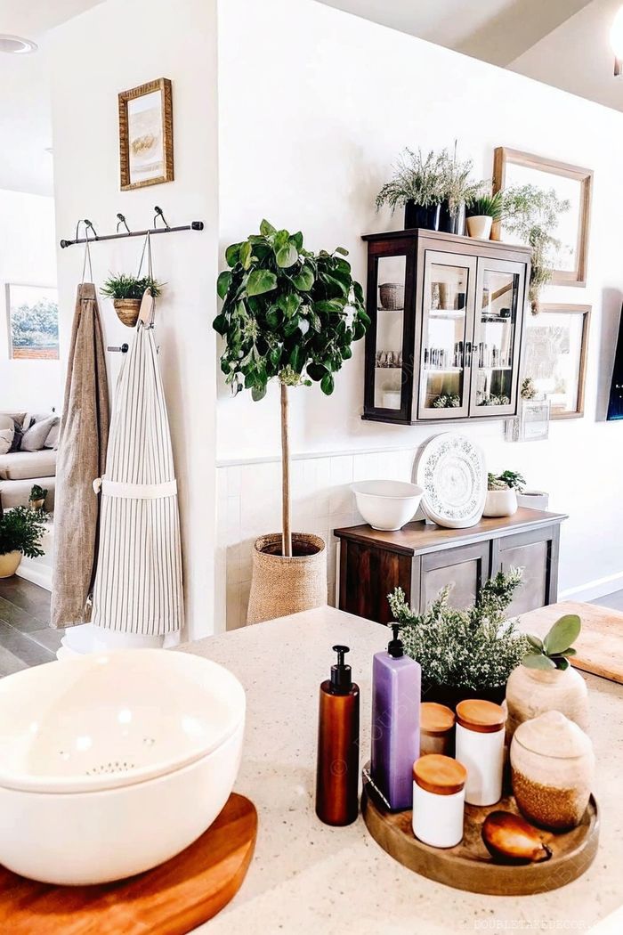 Stylish kitchen featuring aprons on a rod, potted plants, and a wooden sideboard with ceramic dishes and glass storage containers.