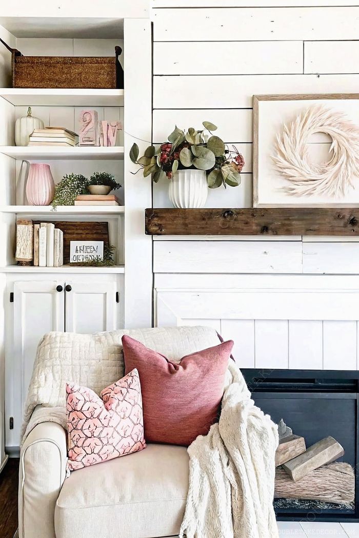Cozy living room with light sofa, pink accent pillows, white shiplap walls, and rustic wooden mantel with curated farmhouse decor elements.