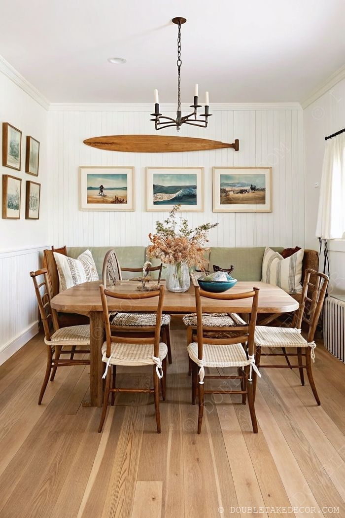 Rustic round farmhouse table with woven chairs and green bench seating under a black chandelier with coastal decor