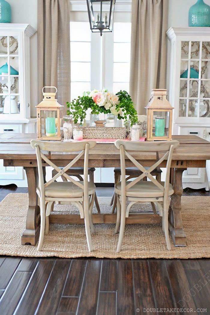 Rustic wooden farmhouse table with chic chairs, adorned with greenery and pink flowers, lanterns, and a soft runner