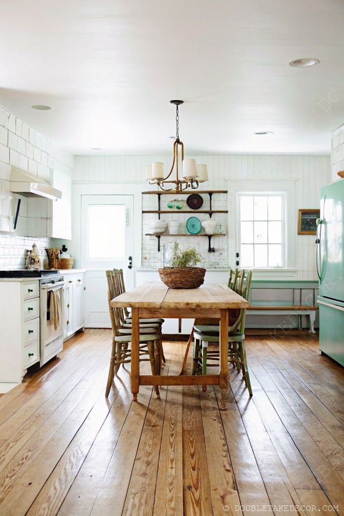 Cozy kitchen with wooden farmhouse table, mismatched chairs, chandelier, and vintage green refrigerator creating rustic charm.