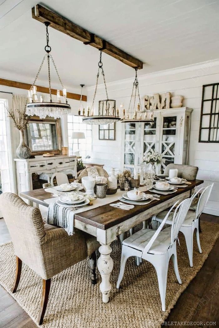 Rustic farmhouse dining table with mixed seating, dual chandeliers, and elegant table settings in a bright, airy space.
