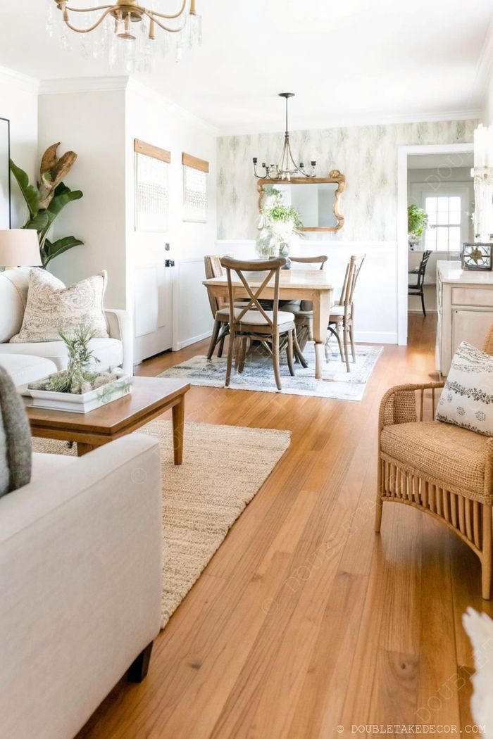 Open-concept space with rustic wooden farmhouse table, crossback chairs, and elegant chandelier in warm, inviting atmosphere.