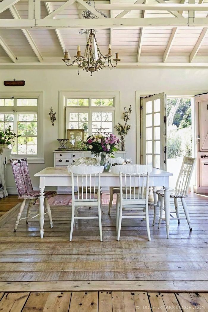 Rustic farmhouse table with mismatched chairs under white-beamed ceiling with chandelier and natural light pouring in.