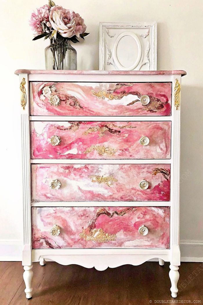 Romantische Kommode mit vier Schubladen – marmoriert in Rosa und Weiß, goldene Akzente, oben steht eine Vase mit Rosen.