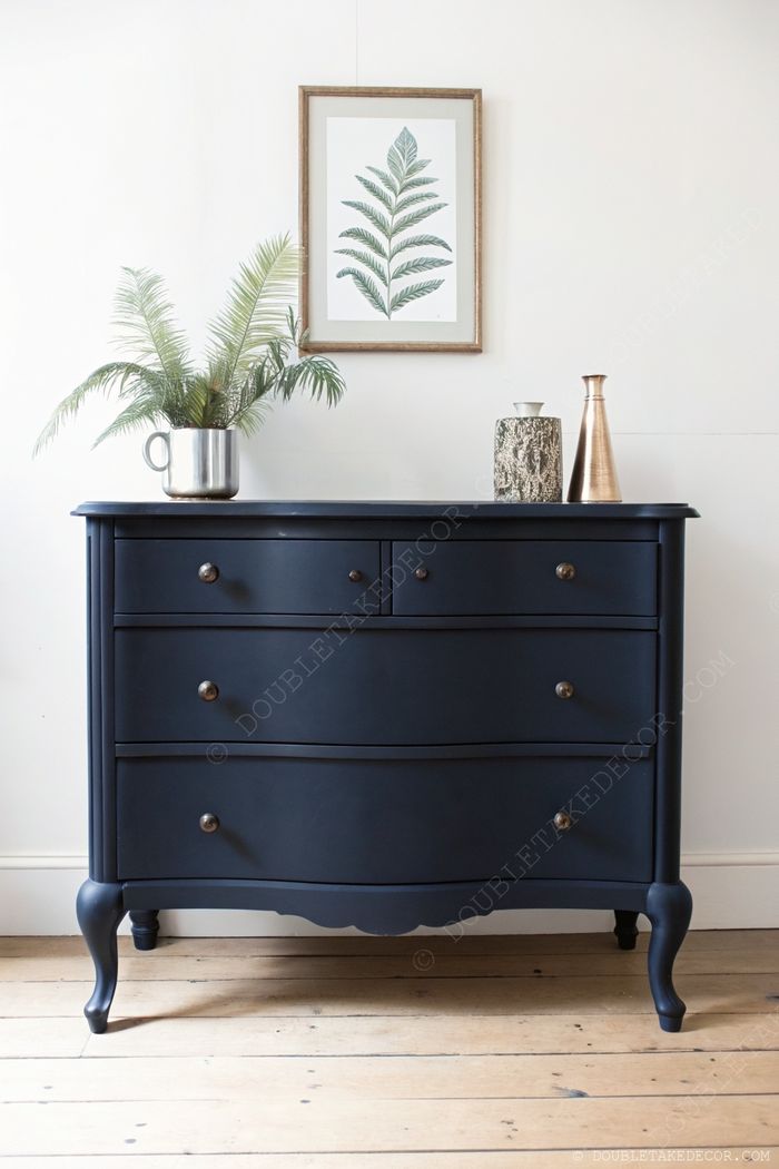 Vintage-Kommode in Marineblau mit fünf Schubladen, dekoriert mit grüner Topfpflanze, Vasen und botanischem Wandbild.